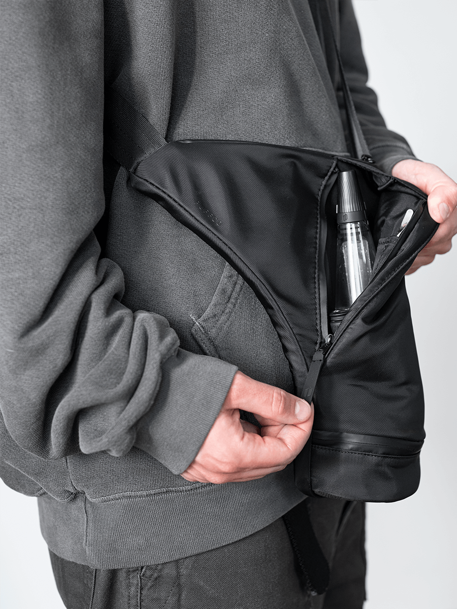 Person wearing Puffco black crossbody dab rig bag and unzipping front compartment