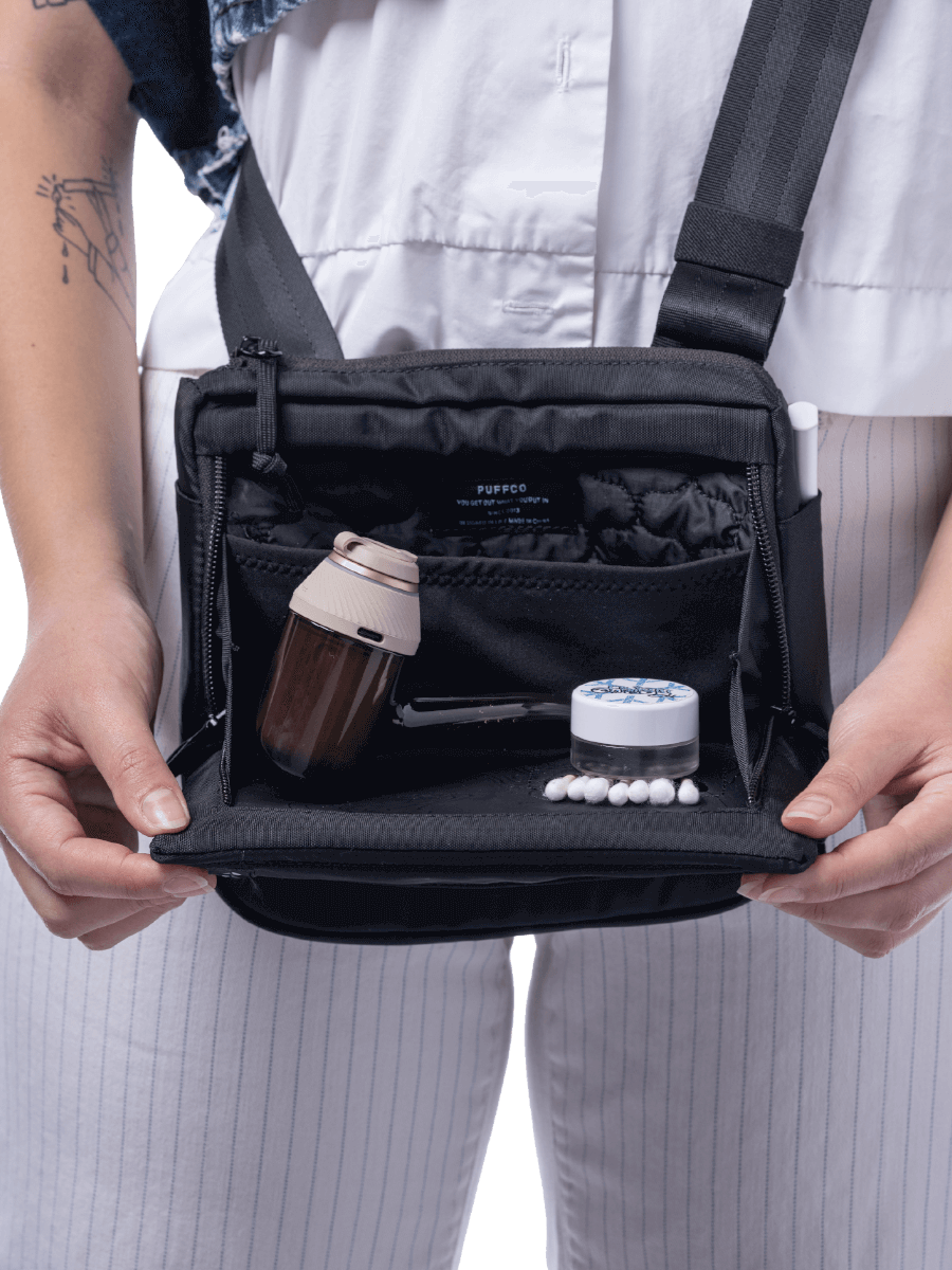 Close up of a person holding open the main compartment with protective padding of black Puffco Proxy bag with pipe and accessories inside
