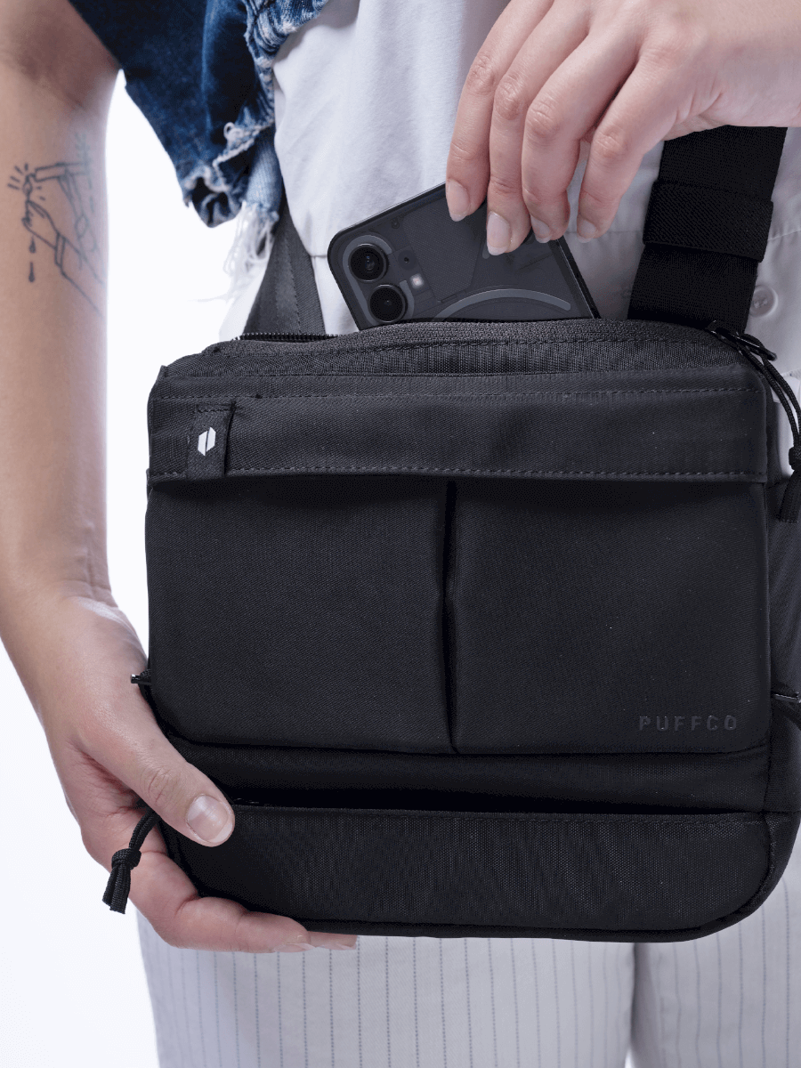 Close up of a person holding a Puffco black Proxy travel bag and placing a cellphone into the back compartment