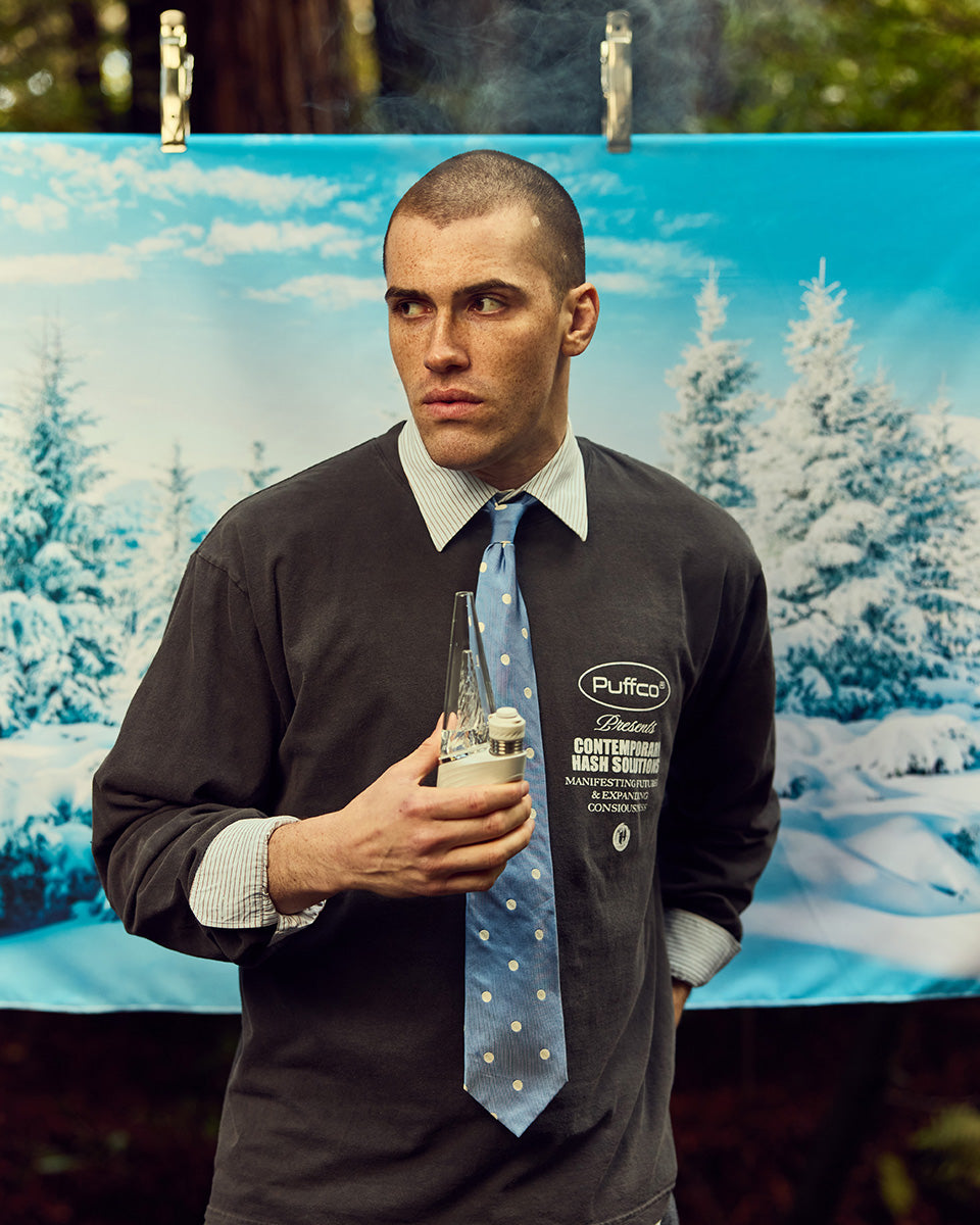 Man wearing puffco long sleeve and a tie, holding Peak device
