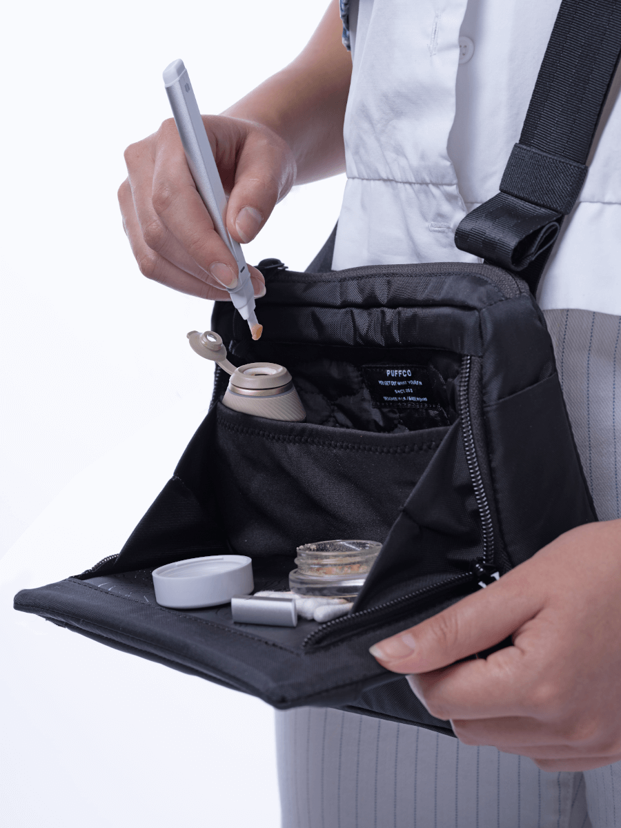 Close up of a person wearing a black Puffco Proxy travel bag with open tray compartment and protective padding filling a beige travel pipe using hot knife