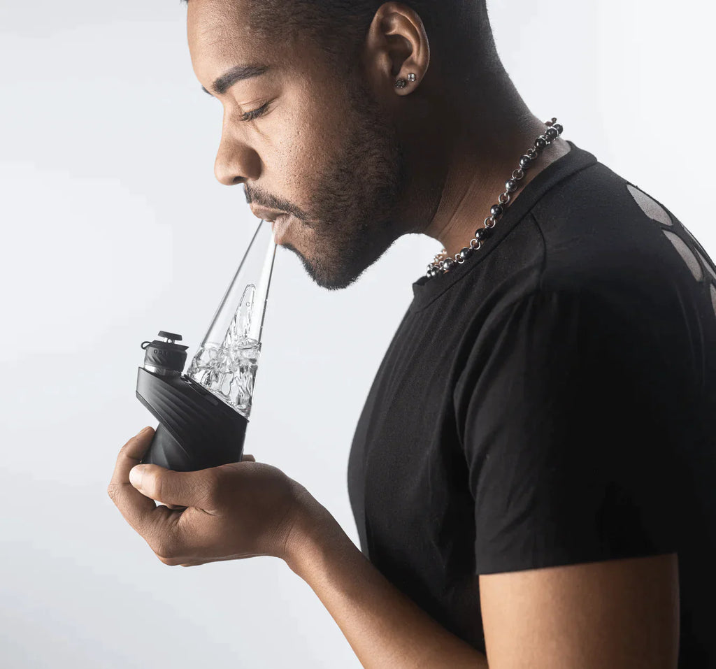 Side shot of a man holding a black Puffco new peak pro with mouth on the mouthpiece