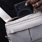 Close up of a person holding a Puffco beige Proxy travel bag and placing a cellphone into the back compartment