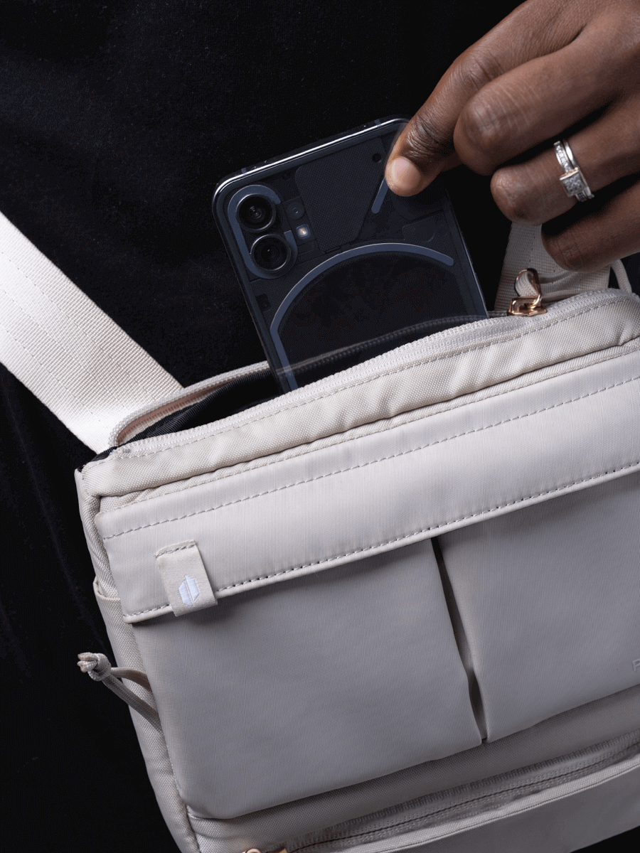 Close up of a person holding a Puffco beige Proxy travel bag and placing a cellphone into the back compartment